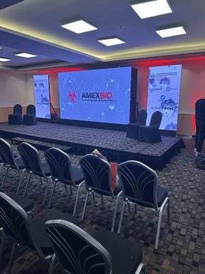 Stage setup for AMEXBIO 2025 with AMEXBIO logo, screens, and branding, taken before the start of a session.