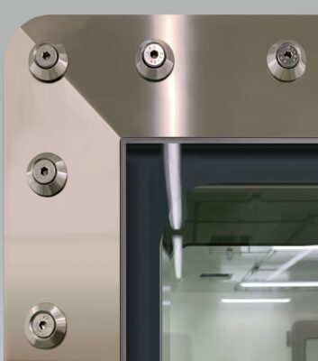 Close-up of a High Containment APR Vision Panel set within a metallic door or window frame, with several round bolts and a glass panel revealing a brightly lit room inside.