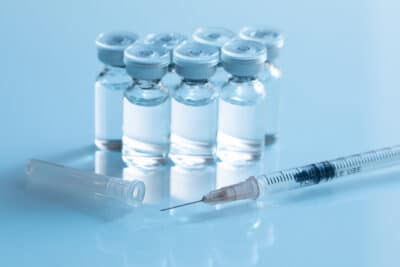 Multiple pharmaceutical vials arranged in a group with a single-use syringe in the foreground, representing sterile drug production facilities served by PBSC laboratory equipment
