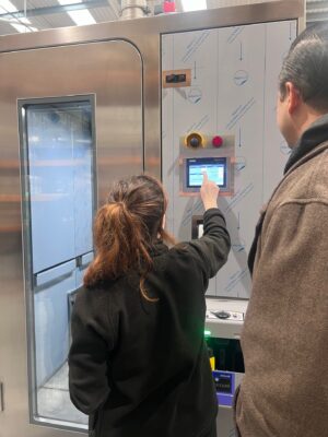 Capricor Therapeutics representative operating the Siemens SIMATIC HMI touchscreen on a PBSC hydrogen peroxide decontamination chamber, with emergency stop and cycle controls visible during factory acceptance testing