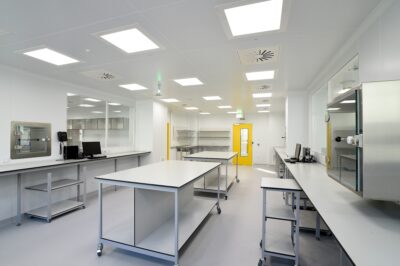 Wide view of a clean, well-lit high containment laboratory interior with mobile workbenches, HEPA ventilation grilles, a pass-through hatch and yellow-framed controlled access door
