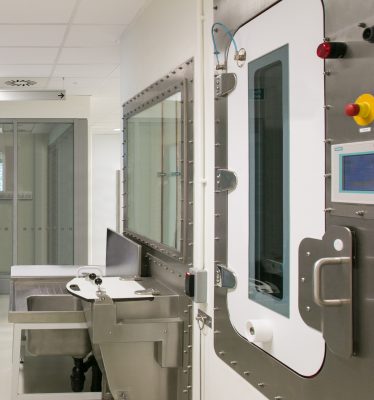 Interior of a high-security lab with reinforced stainless steel equipment, airlock door, and sealed observation window.