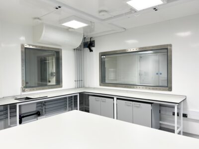 A clean, modern laboratory featuring a High Containment APR Vision Panel, with white walls, large windows, overhead lighting, and counters with cabinets and sinks.